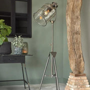 Tripod base industrial style brass floor lamp with a glass shade over the bulb