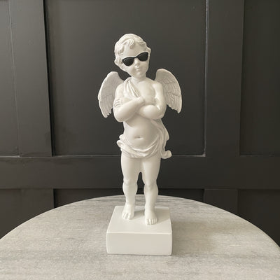 White small cherub statue with black sunglasses and his arms crossed