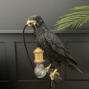 Black crow on a stick table lamp with a bulb in it's mouth