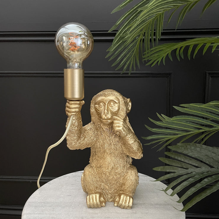 Gold sitting monkey lamp holding a light bulb