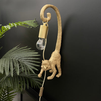 Gold hanging monkey wall light with a bulb dangling off it's tail