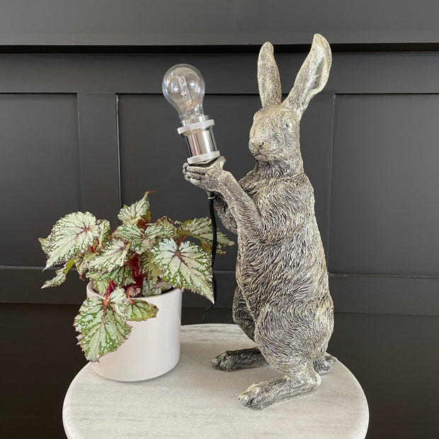 Silver rabbit table lamp holding a bulb
